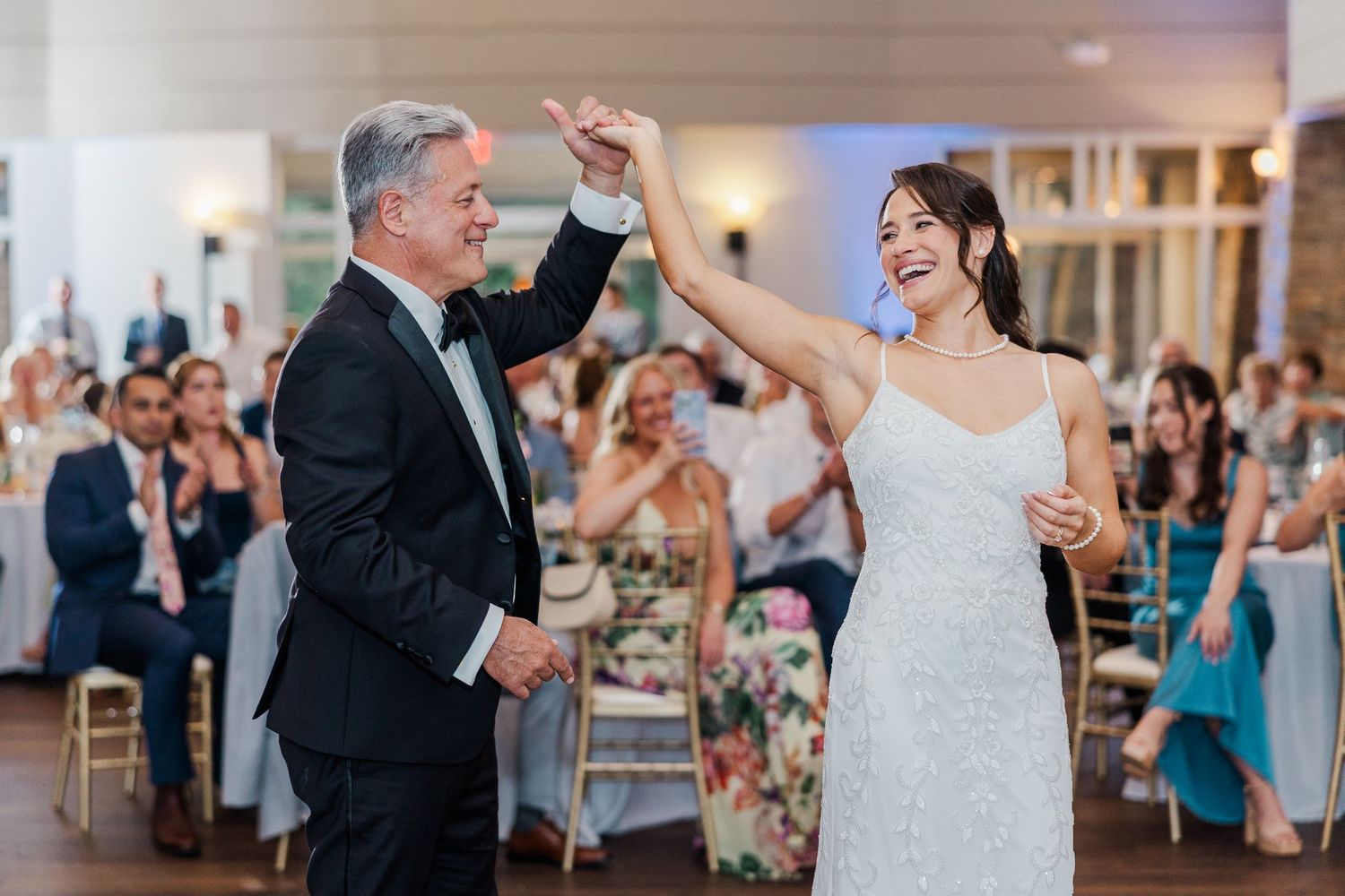 Bride in white gown dancing with groom in tuxedo at elegant wedding reception with guests applauding.
