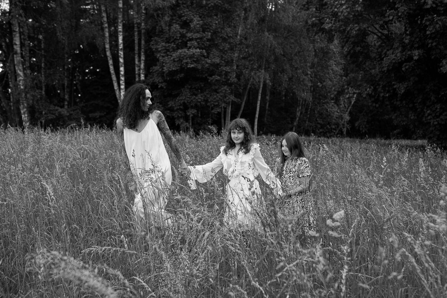 Family portrait of parents and two children posing together in casual black and white outfits against a gray background.