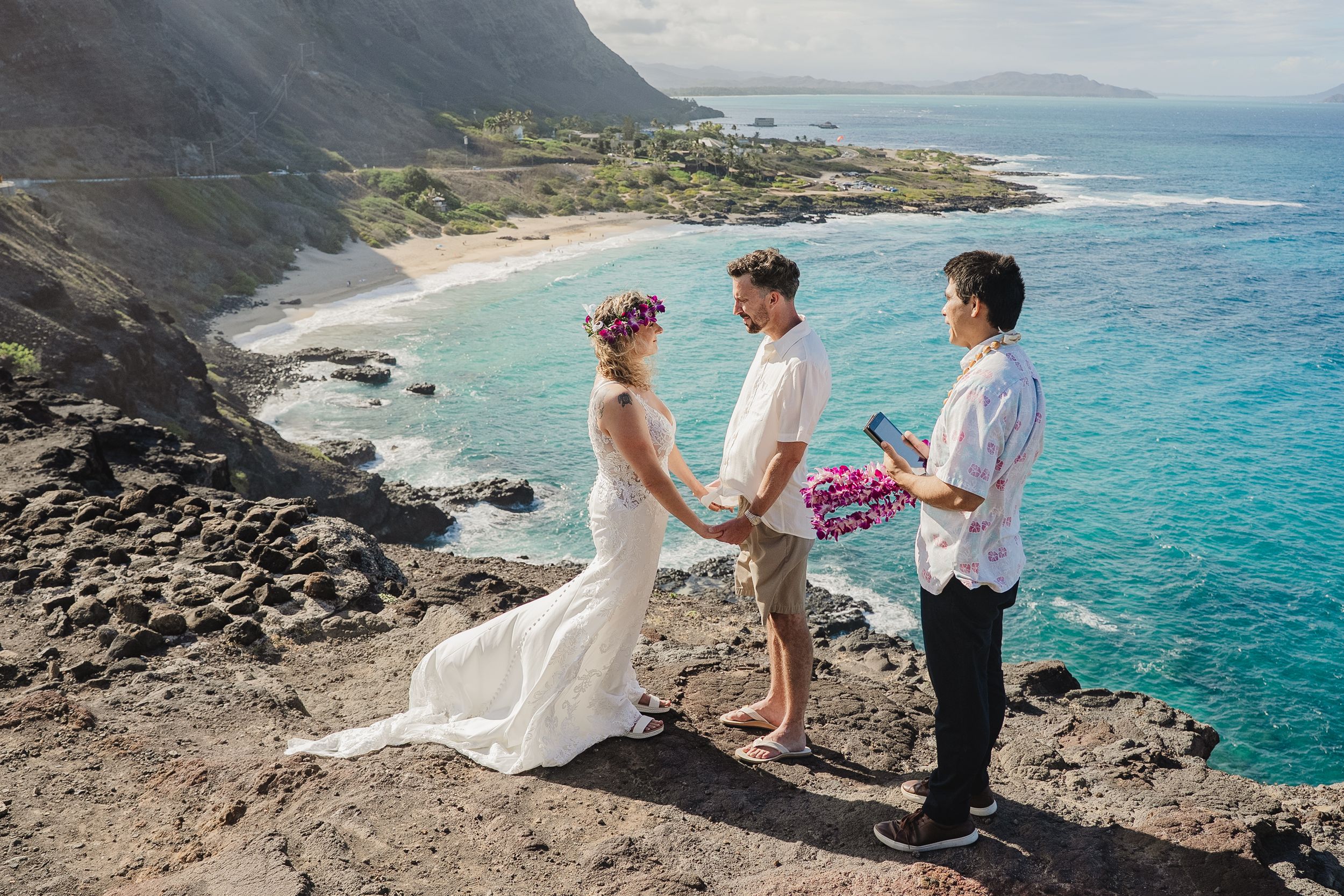 Couple exchanges vows during a cliffside elopement ceremony in Hawaii with stunning ocean and mountain views.