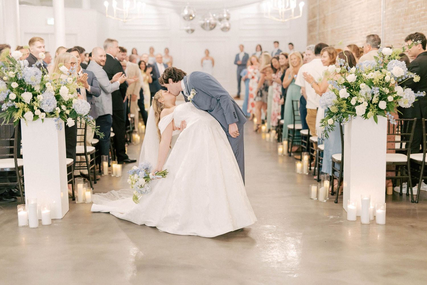 Bride and groom share a romantic dip kiss at the altar during their elegant indoor wedding ceremony.
