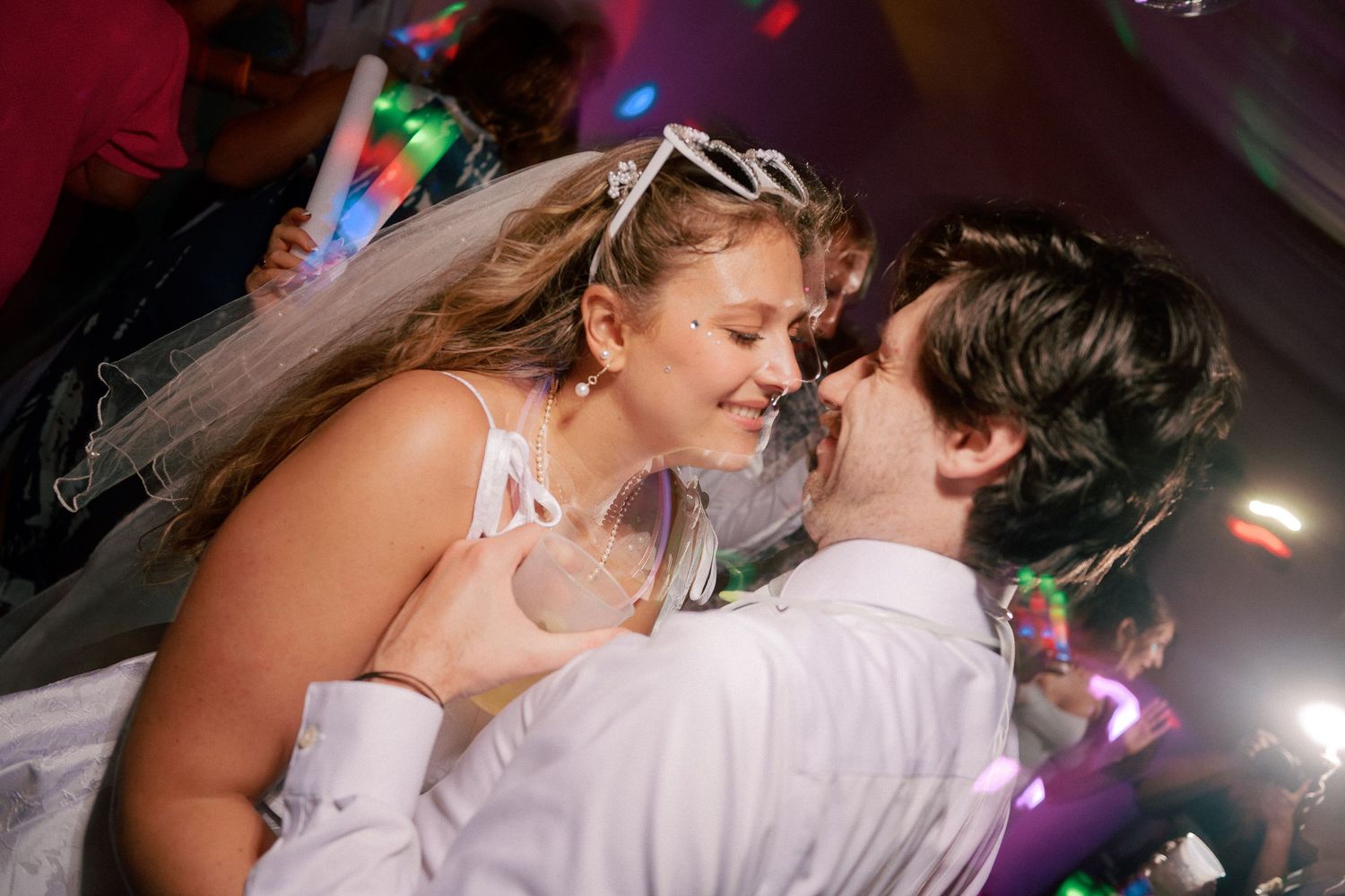 Bride and groom sharing a romantic dance at a wedding reception with colorful party lights in the background.