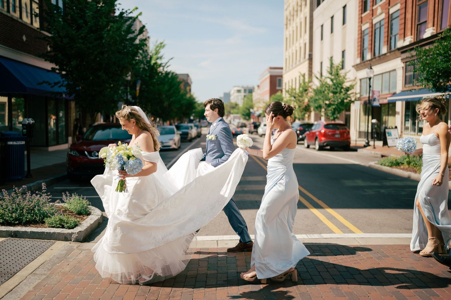 Wedding party crossing a city street, bride's gown flowing in the breeze with bridesmaids and groomsman.