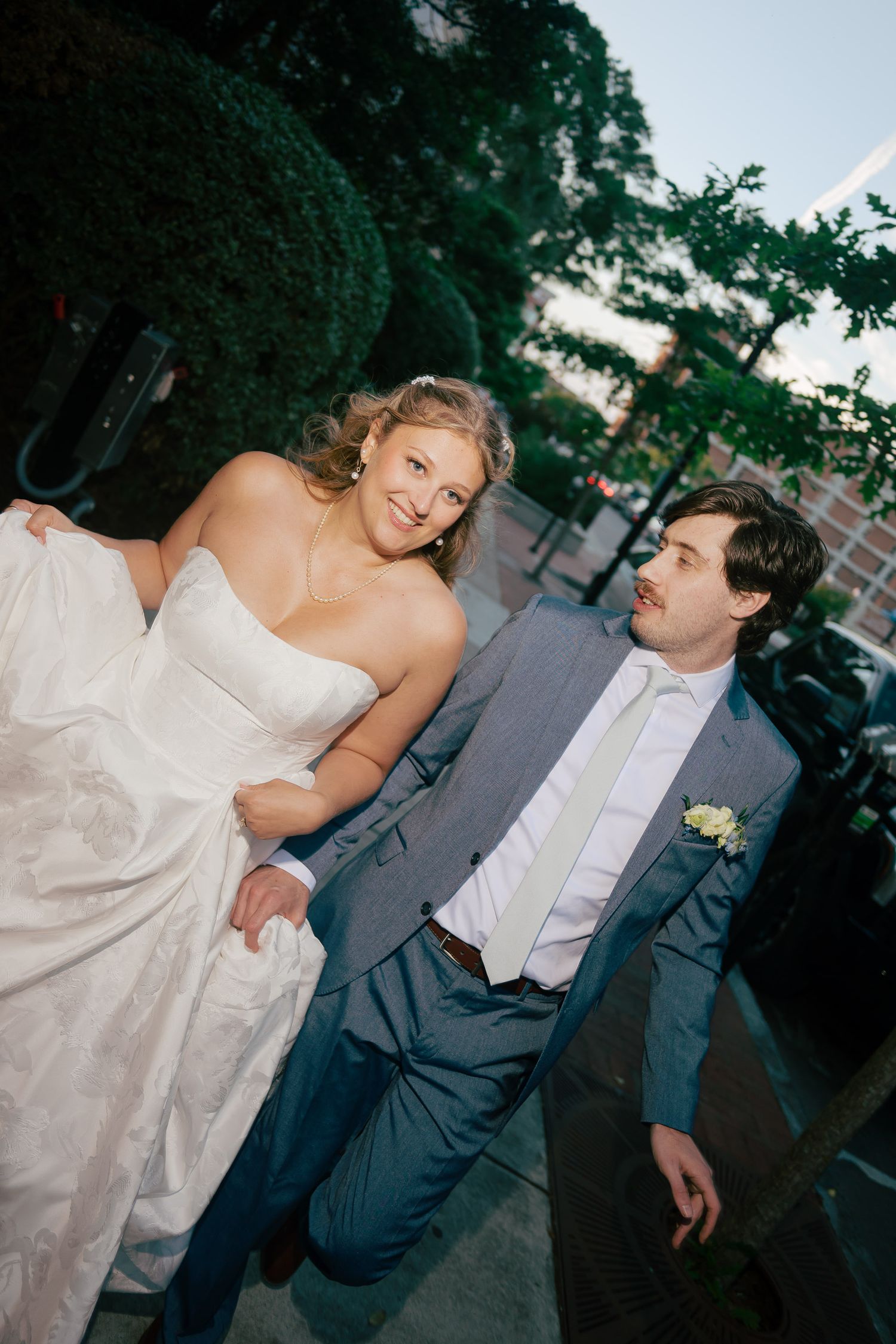 Bride in white strapless gown and groom in gray suit walking together outdoors at their wedding.