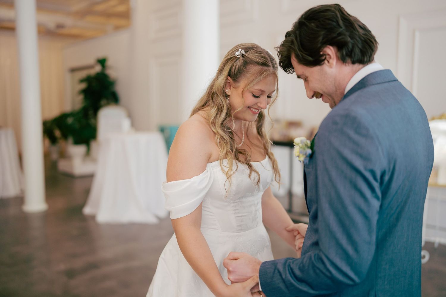 Bride and groom sharing intimate moment during wedding ring exchange in elegant white reception venue.