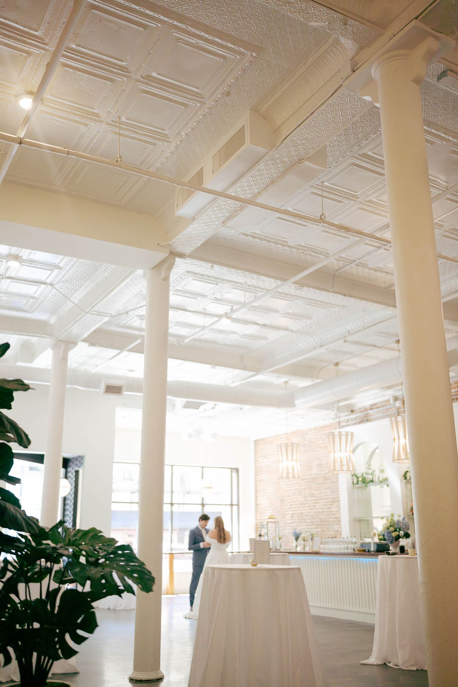 Elegant event venue with ornate white tin ceilings, tall columns, and draped tables set for a wedding reception.
