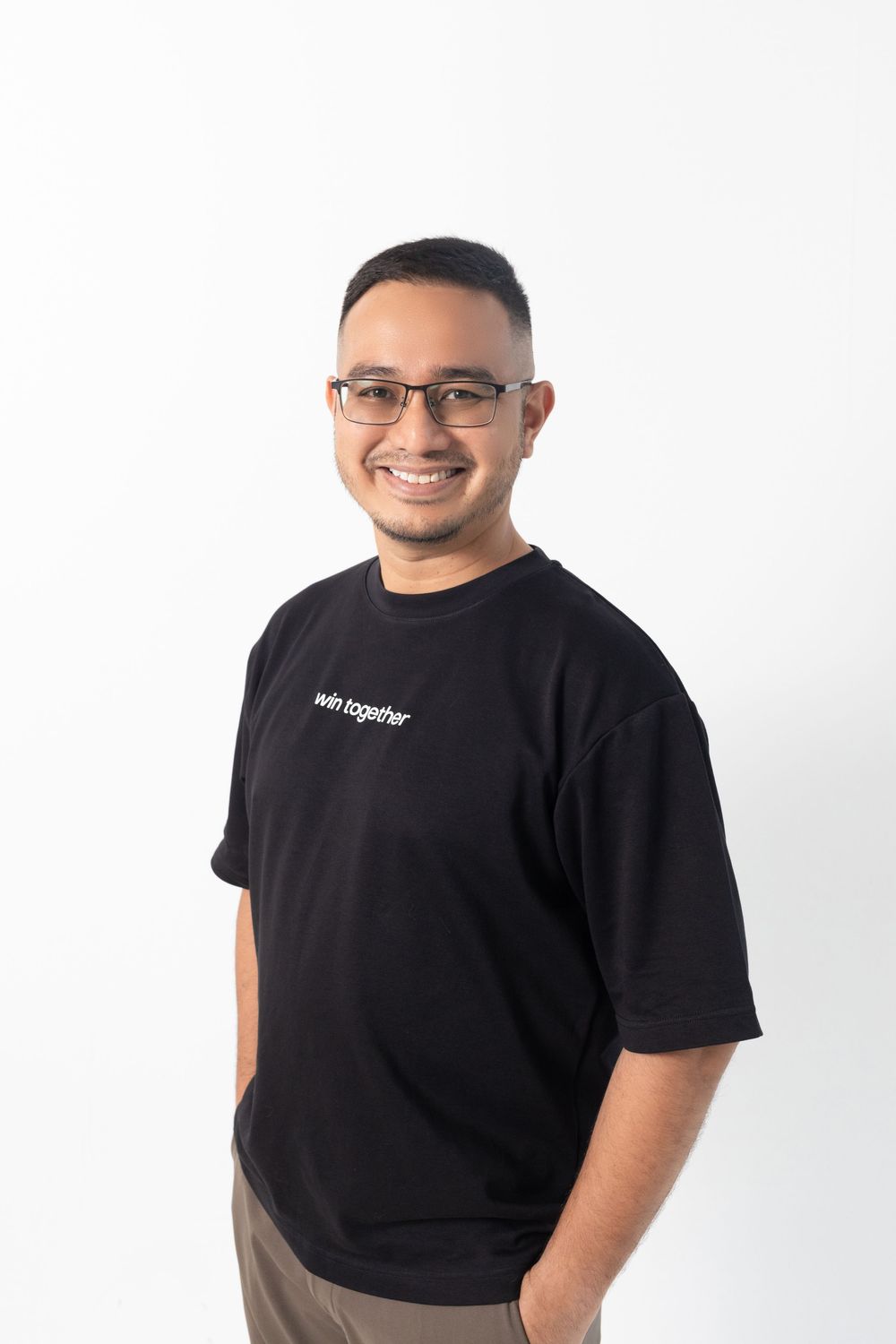 Smiling man wearing glasses and black 'win together' t-shirt posing against white background.