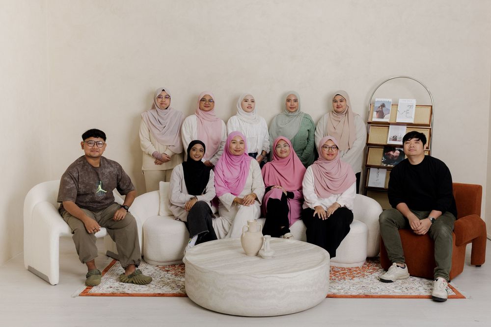 Group of people in hijabs posing together on white sofas in a modern, minimalist room with warm decor.