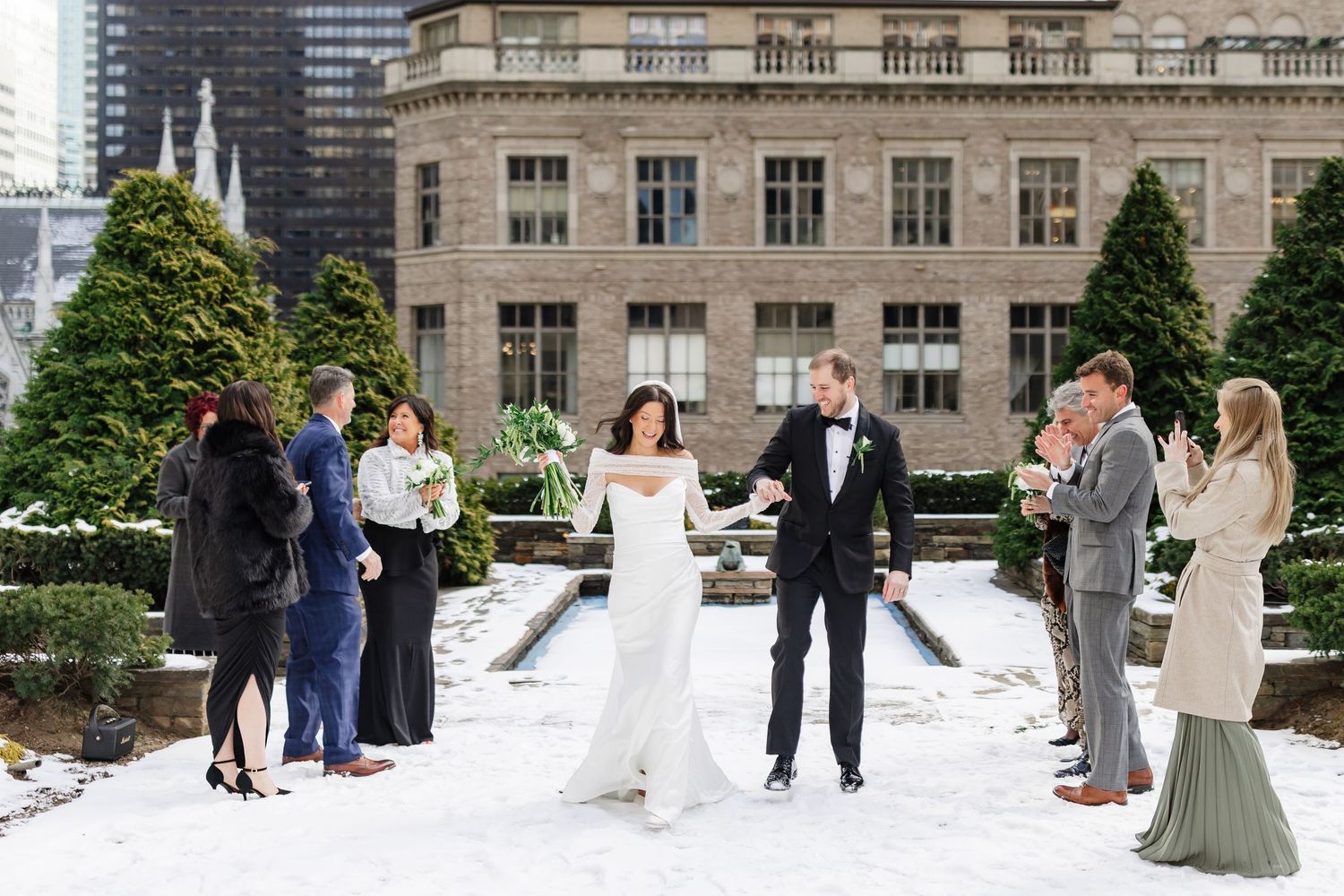 Bride and groom walk through snowy outdoor venue with guests lining the aisle at a winter wedding in New York City.