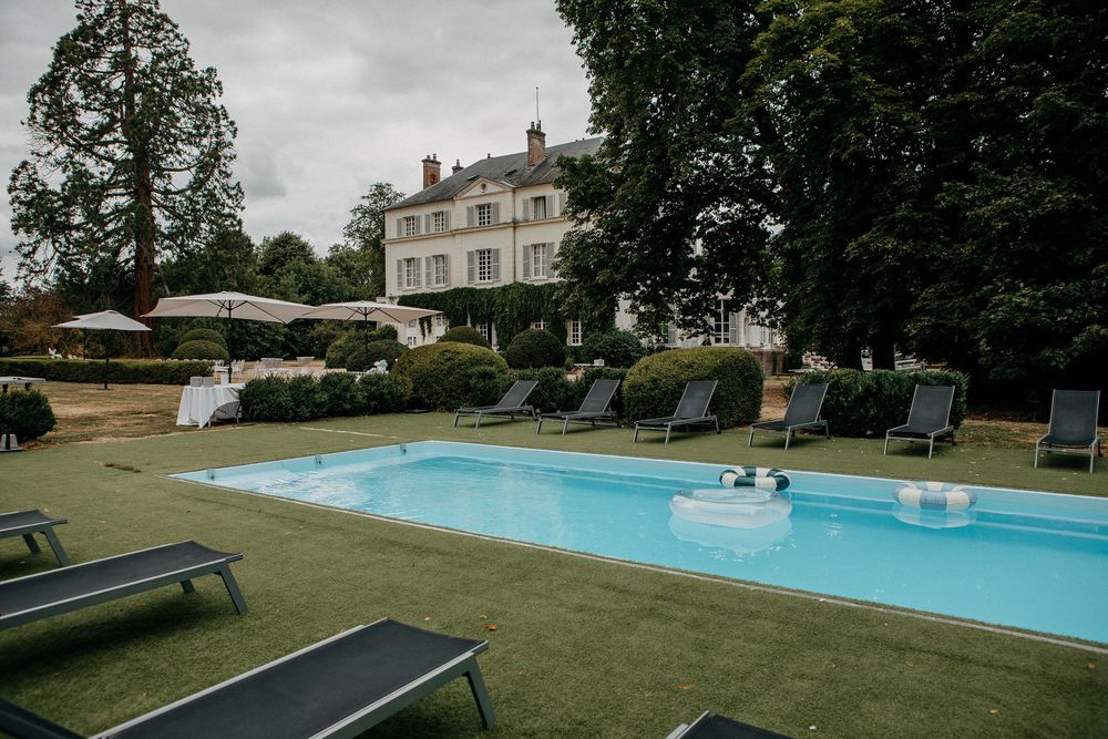 Elegant French château with a pristine outdoor swimming pool surrounded by lounge chairs on a manicured lawn.