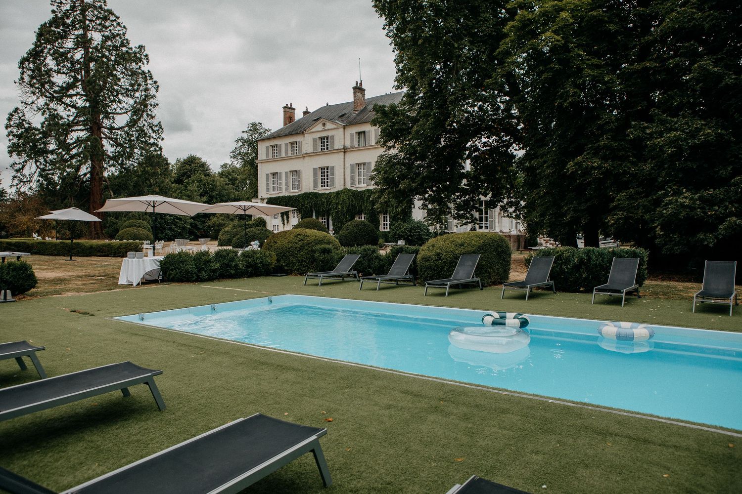 Elegant French château with a pristine outdoor swimming pool surrounded by lounge chairs on a manicured lawn.