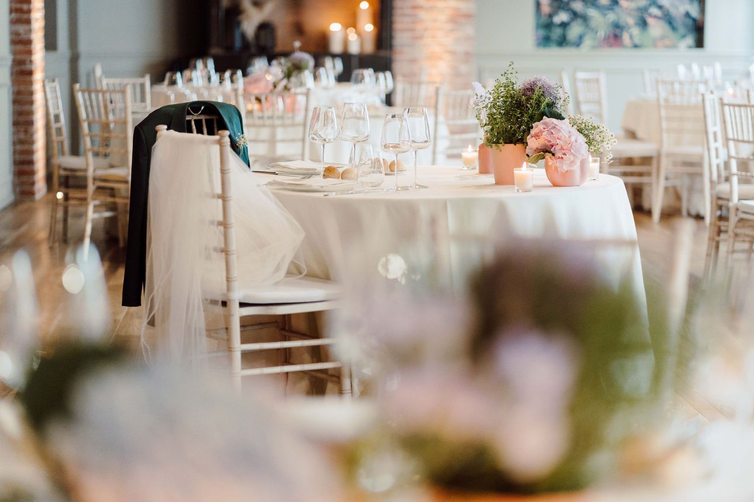 Elegant wedding reception venue with white tablecloths, chiavari chairs, floral centerpieces, and soft natural lighting.