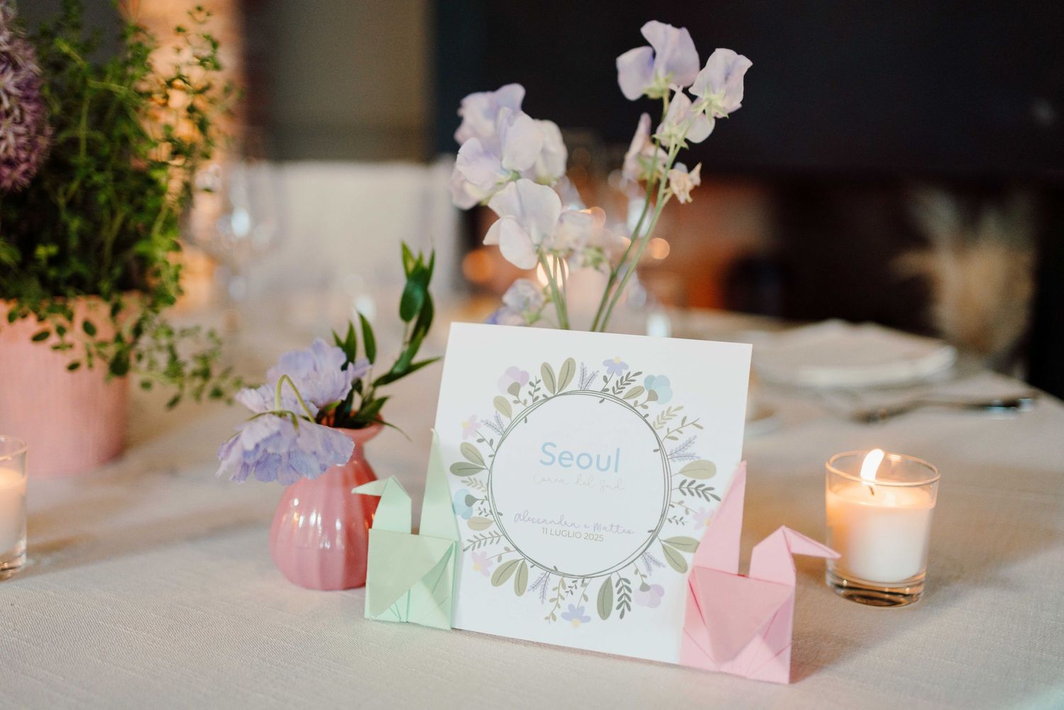Elegant wedding table setting with floral centerpiece, origami decor, candle, and a Seoul place card.