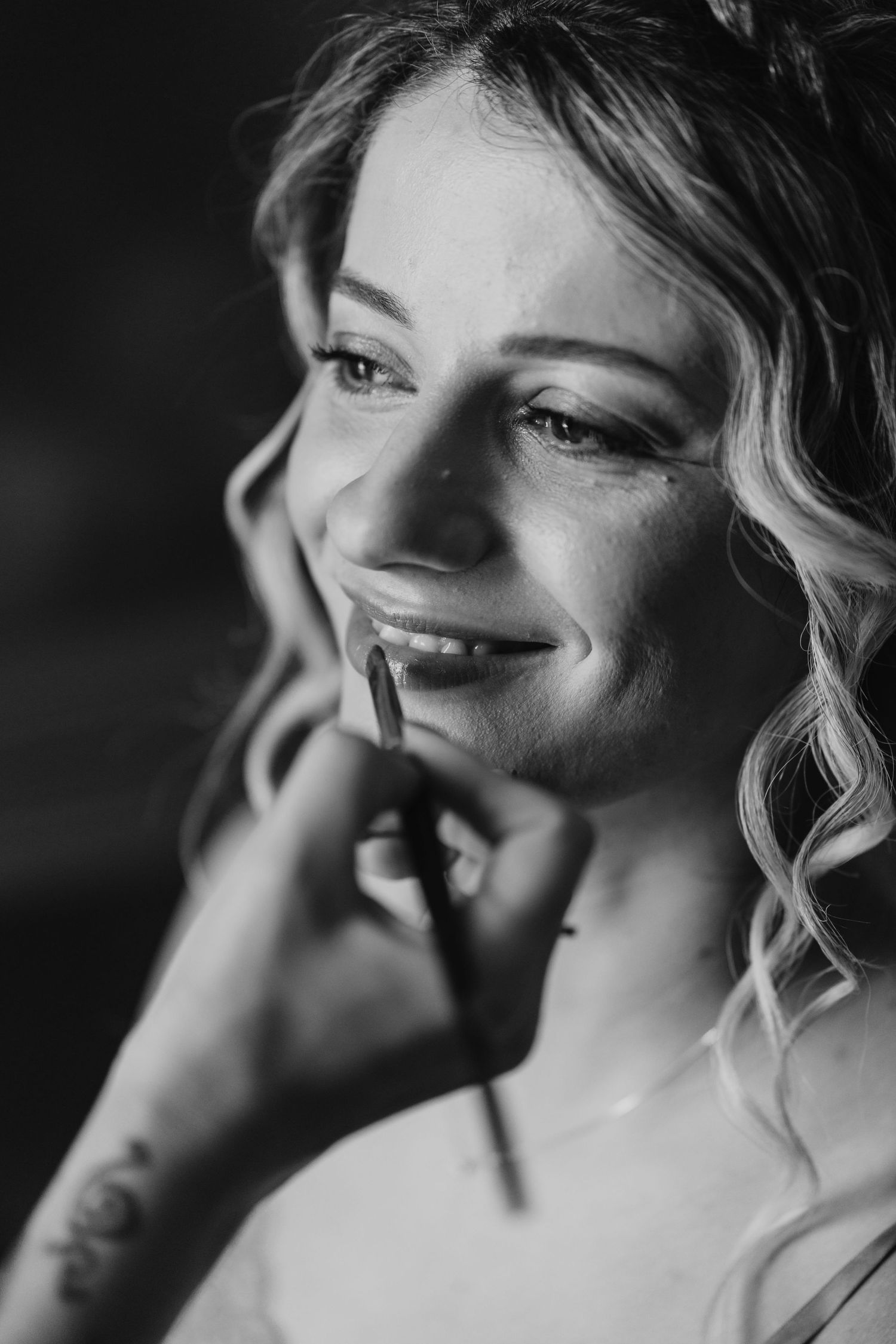 Black and white portrait of a smiling bride getting her makeup applied by a makeup artist.