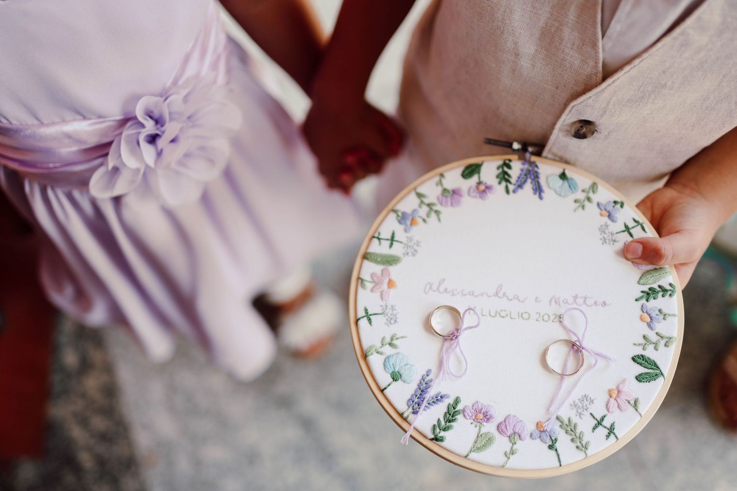 Embroidered hoop wedding ring bearer pillow with floral design held by flower girl in lavender dress.