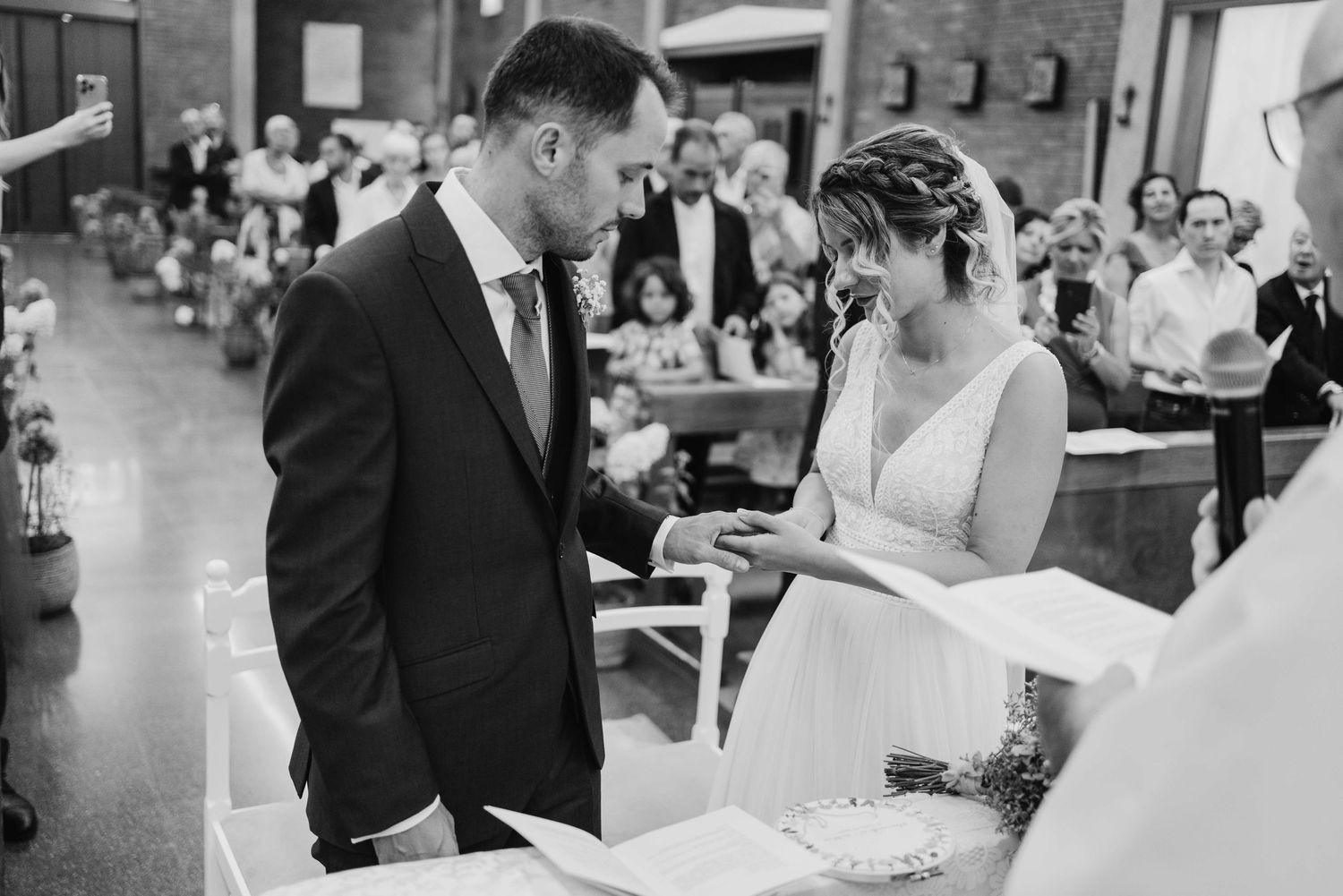 Black and white photo of a bride and groom exchanging vows at a church wedding ceremony altar.