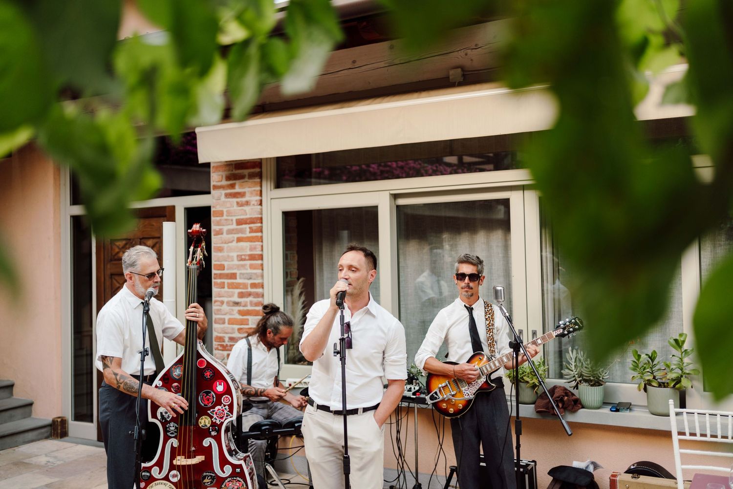 Live band performing outdoors at a wedding, featuring upright bass, guitar, and vocalist in white shirts and ties.