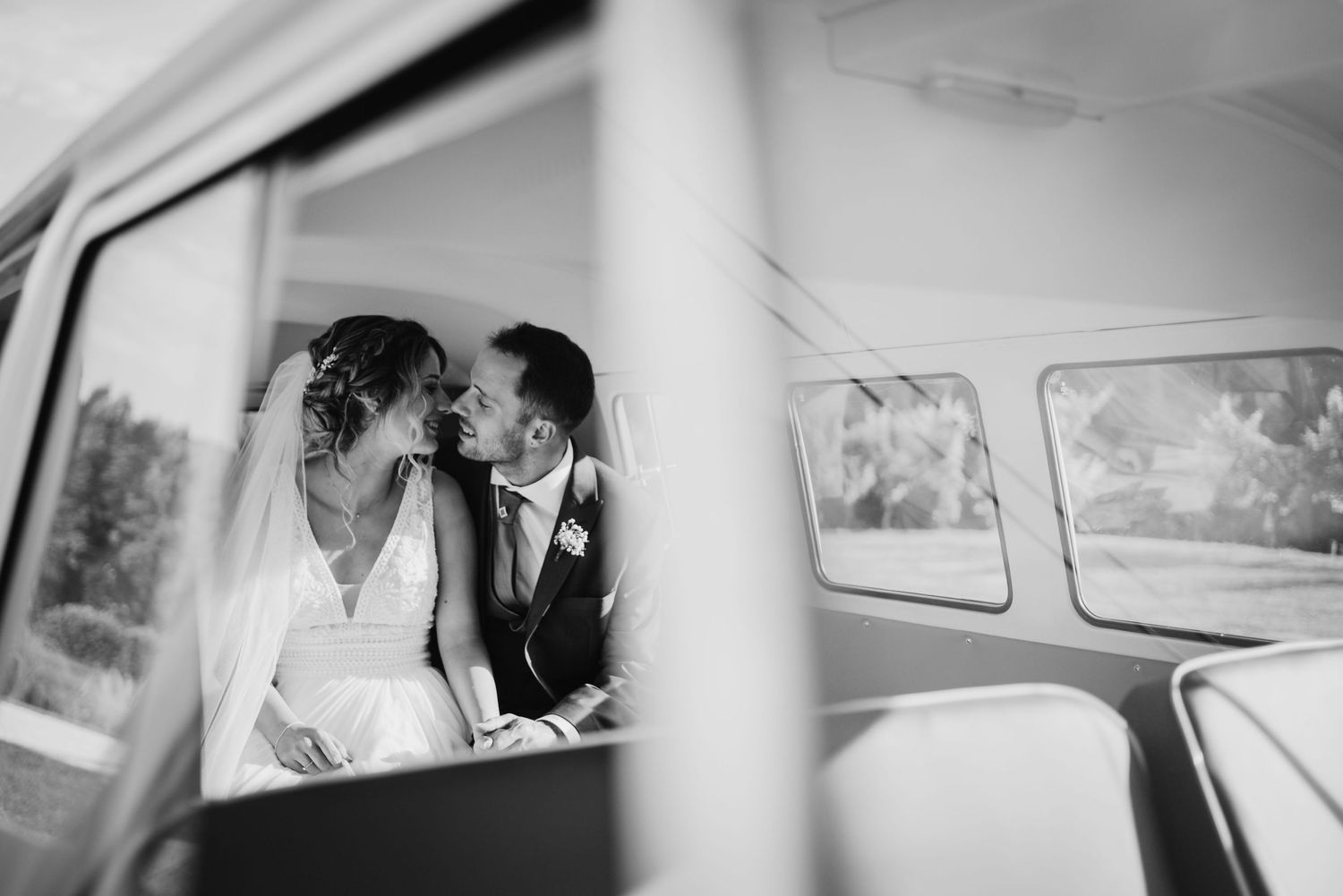 Black and white photo of a bride and groom sharing a romantic moment inside a vintage VW camper van on their wedding day.