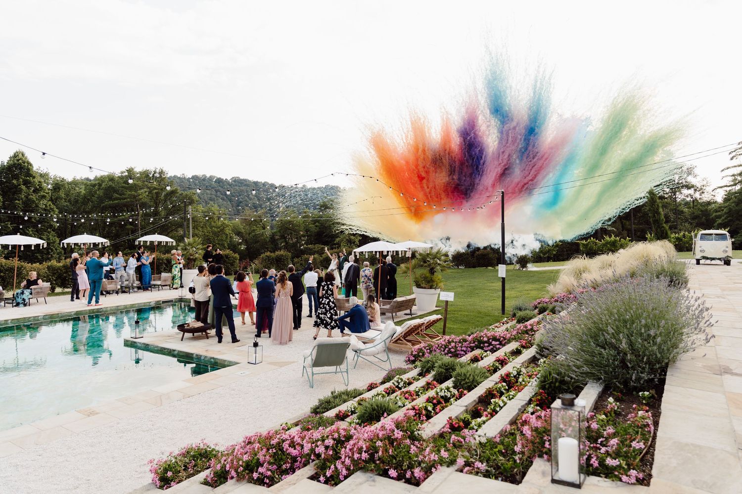 Colorful powder explosion at an outdoor wedding reception near a pool with lush garden landscaping.