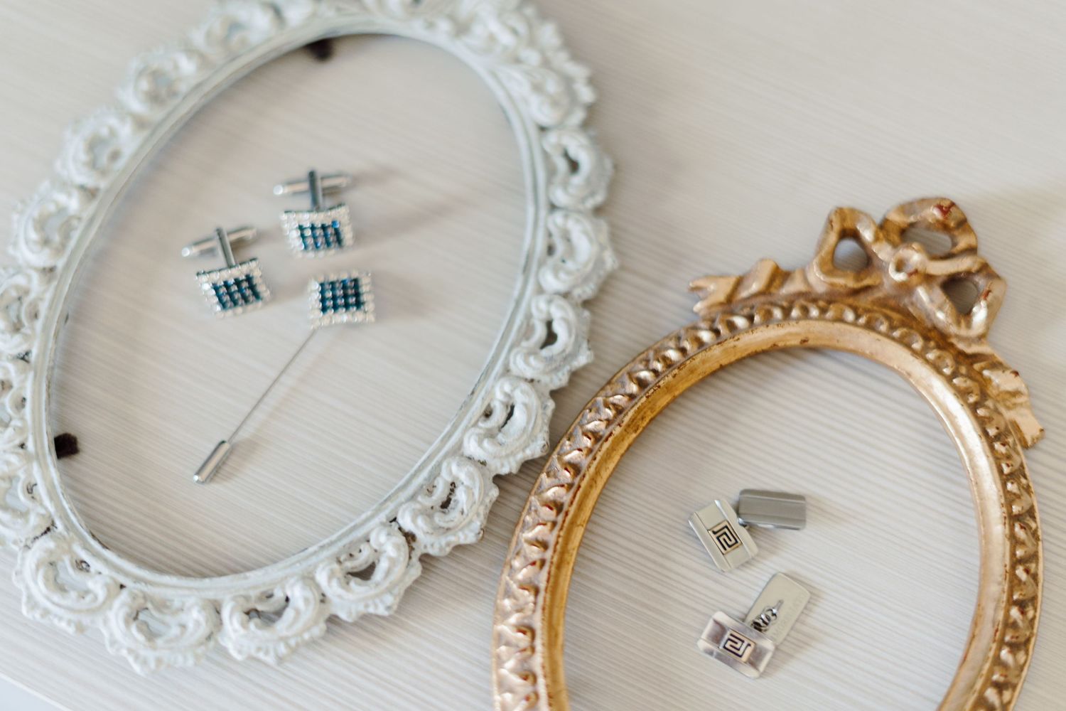 Two ornate picture frames displaying elegant cufflinks and a tie pin on a white surface.