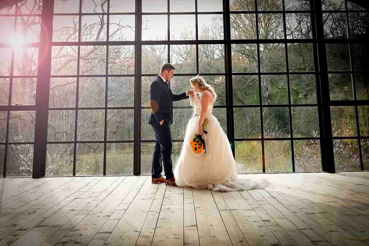 Bride and groom holding hands in elegant venue with large windows and hardwood floors on their wedding day.