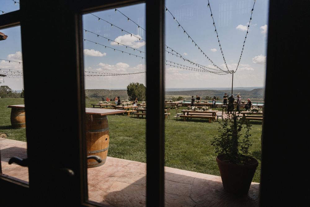 View through glass doors of a winery patio with string lights, barrel decor, and scenic valley views.