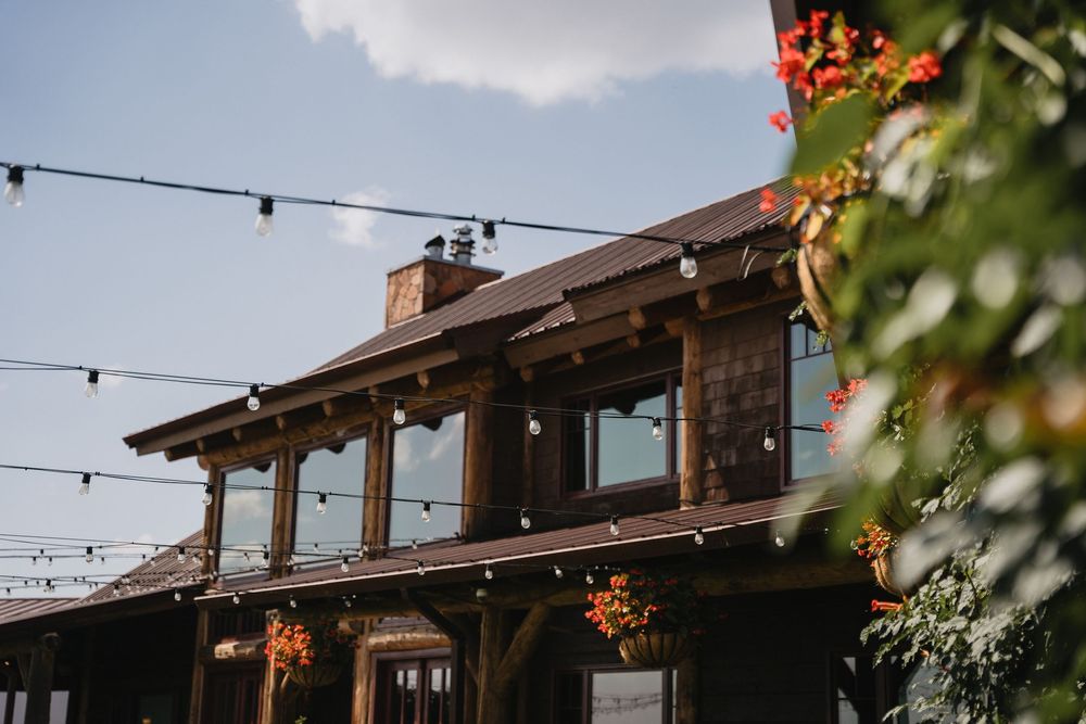 Rustic barn wedding venue with string lights and colorful flowers under blue sky.