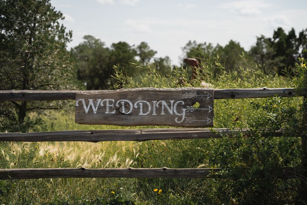 Rustic wooden wedding sign with arrow on a fence surrounded by lush green meadow.