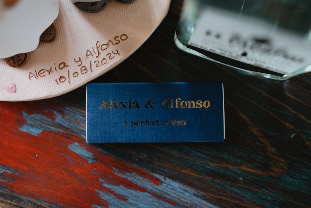 Navy blue matchbox with gold foil text reading Alexia & Alfonso a perfect match, displayed on a colorful wooden surface.