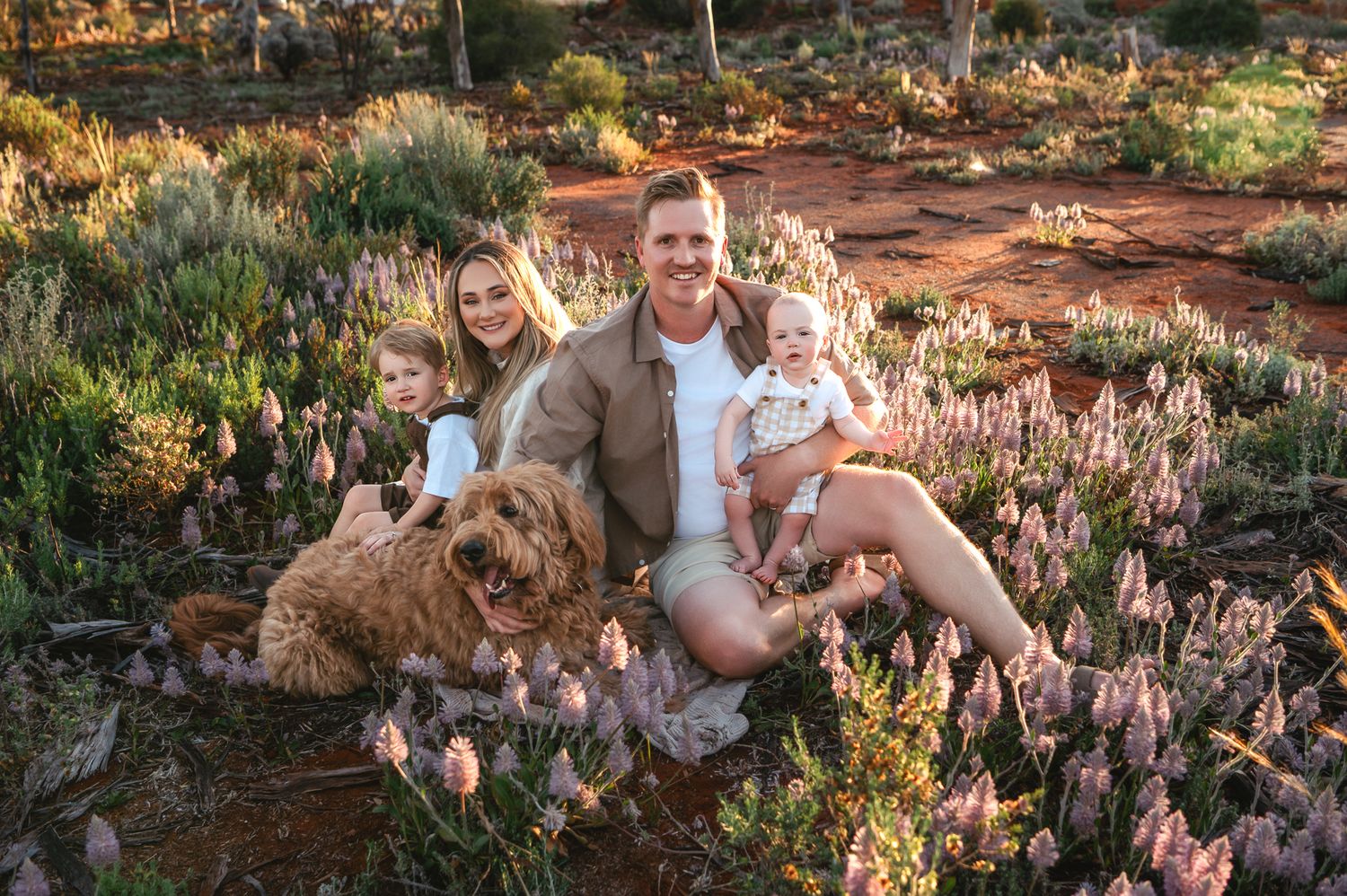 Happy Asian family of three posing outdoors in golden hour light among desert shrubs, parents holding toddler daughter.