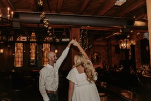 Couple dancing together in a rustic bar venue, woman in white dress being twirled by partner under warm ambient lighting.