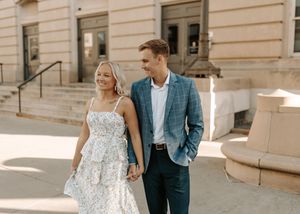 Happy couple walking hand in hand outdoors, woman in floral dress and man in blue blazer, sunny day.