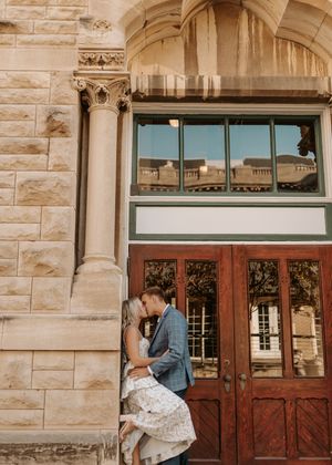 Couple sharing a romantic kiss in front of ornate wooden doors of a historic stone building.