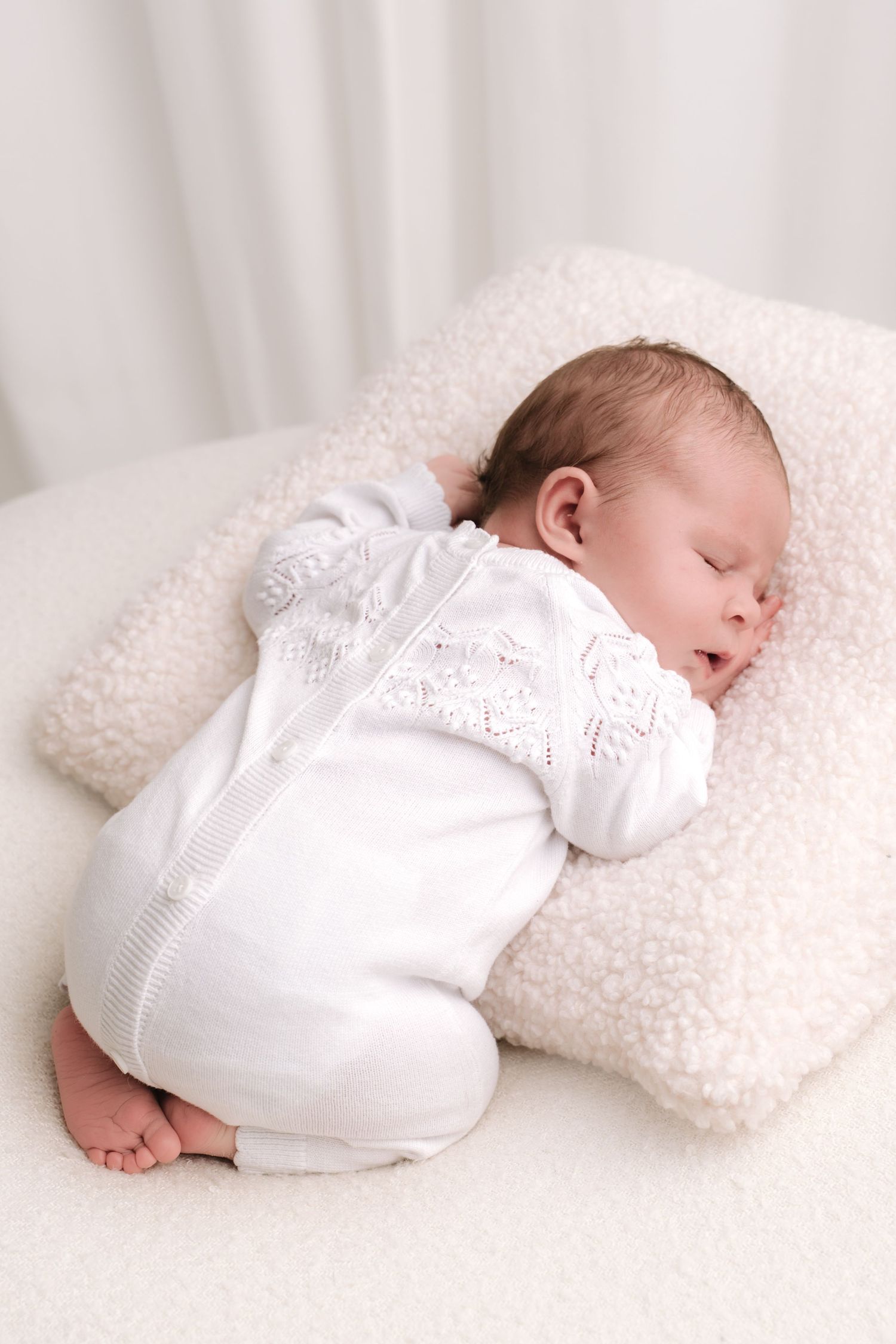Pregnant woman in floral embroidered cream maxi dress cradling baby bump, barefoot on beige background.