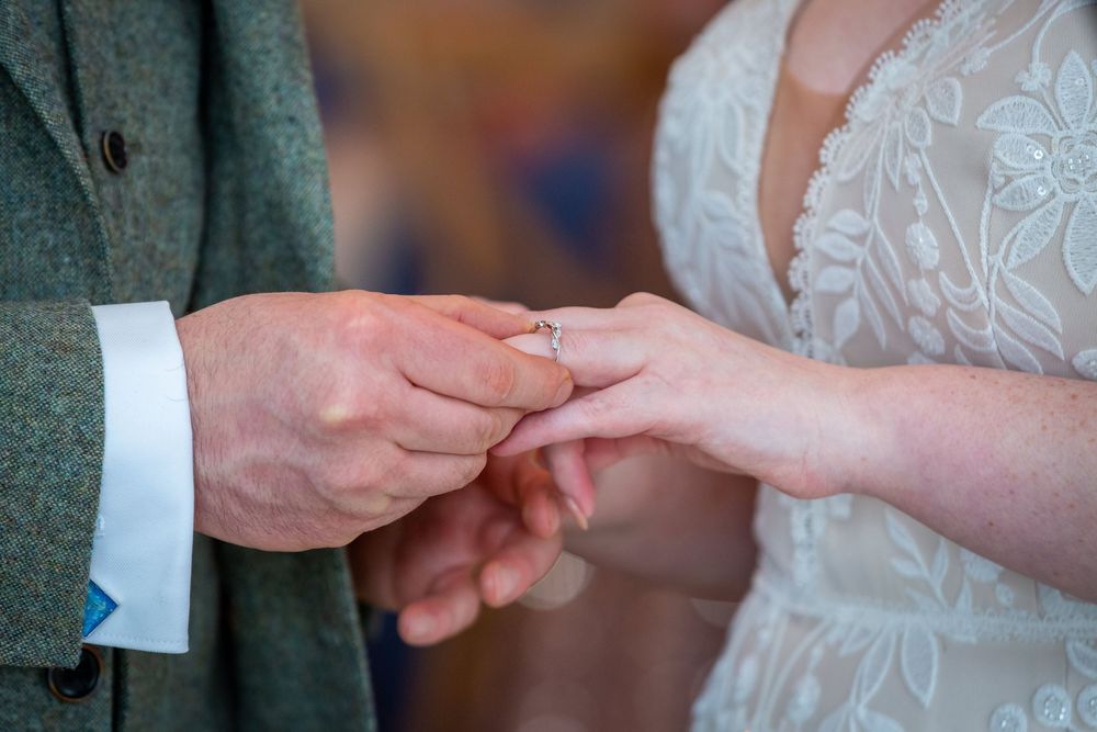 Close-up of a bride placing a wedding ring on the groom's finger during a wedding ceremony.