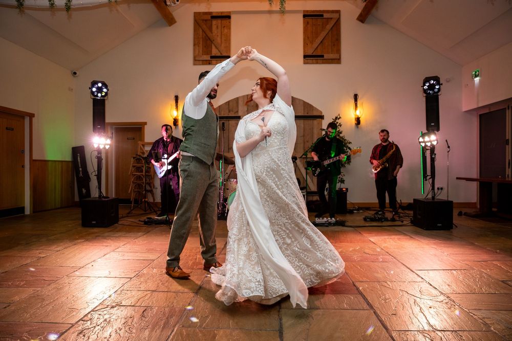 Bride and groom share first dance at wedding reception with live band performing on stage in elegant venue.