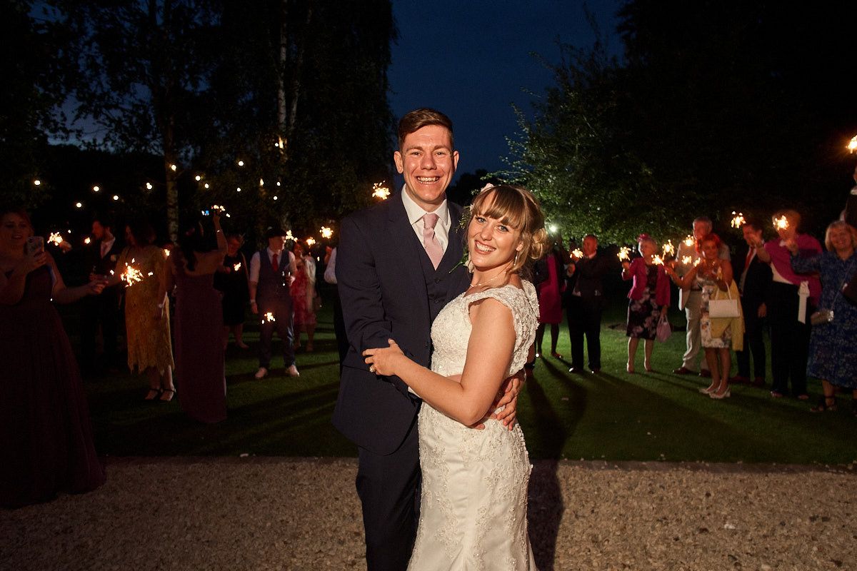 A couple shares a romantic moment at their nighttime wedding reception surrounded by sparklers and guests.