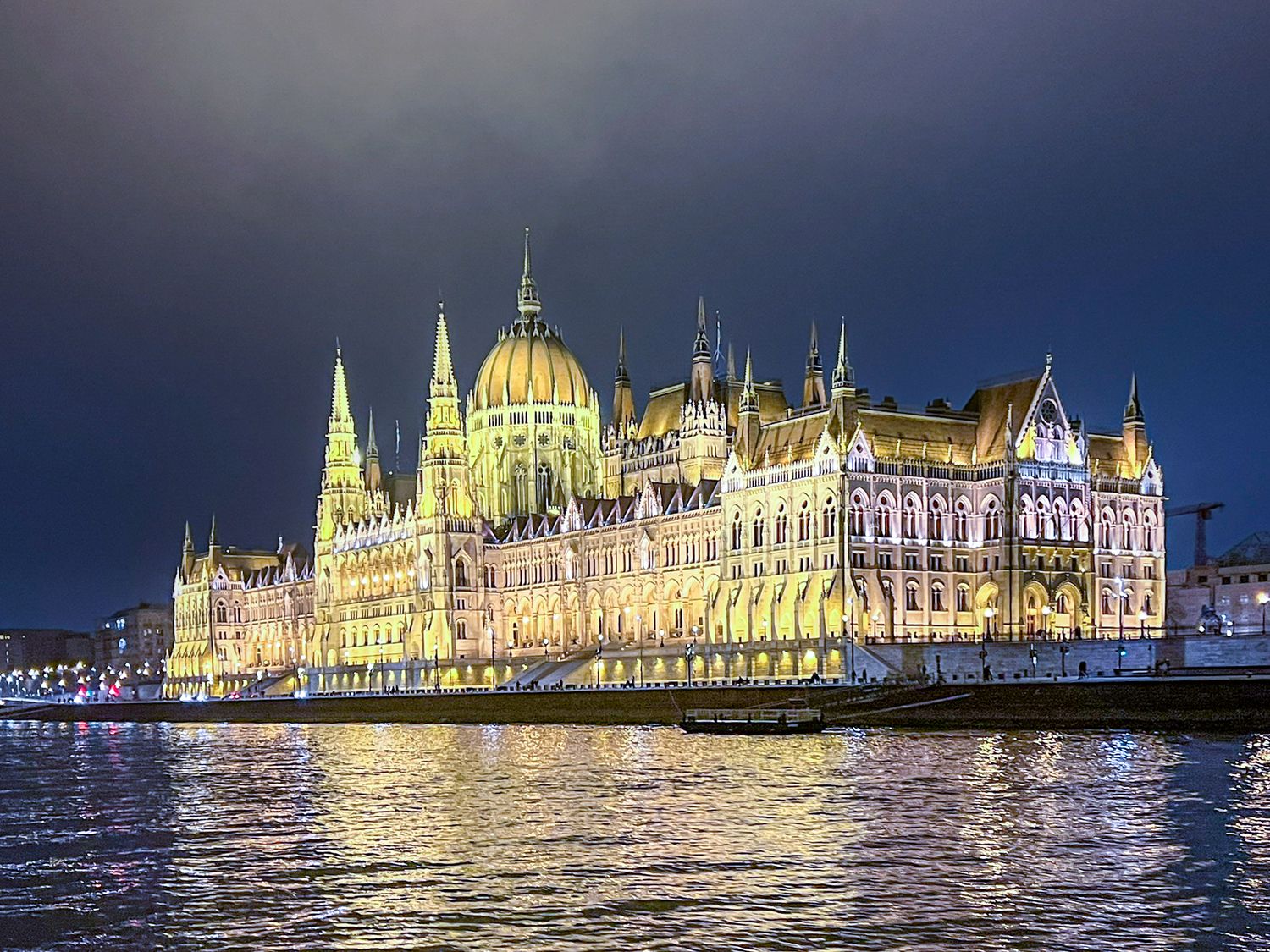 Illuminated Hungarian Parliament Building reflecting on the Danube River at night in Budapest.