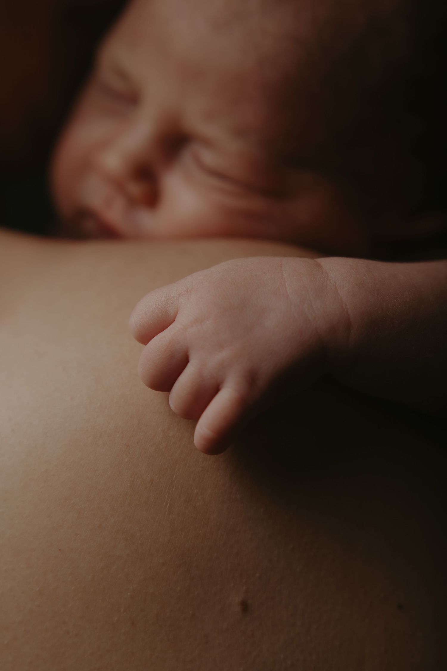 Close-up of a sleeping newborn baby's tiny hand resting gently on a parent's skin.
