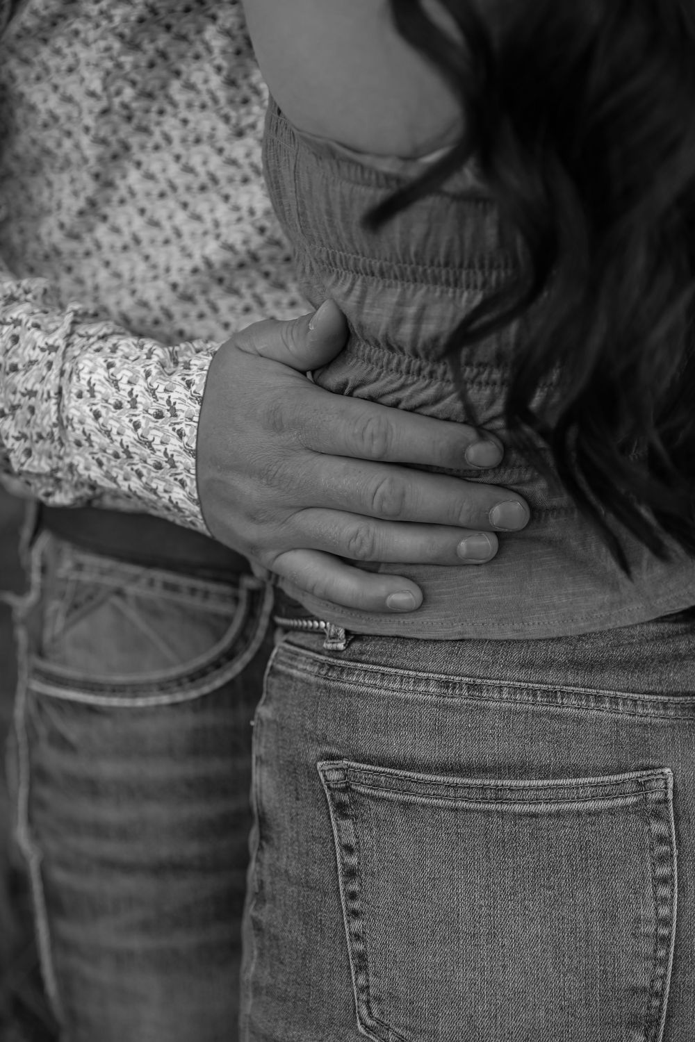 Black and white photo of a couple embracing, with a man's hand resting on a woman's waist in jeans.