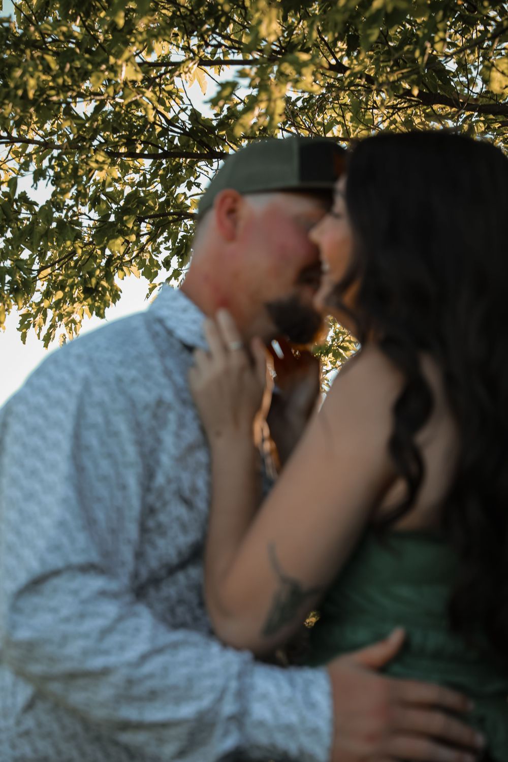 Couple sharing a romantic kiss under a golden-lit tree at sunset, woman holding man's face gently.