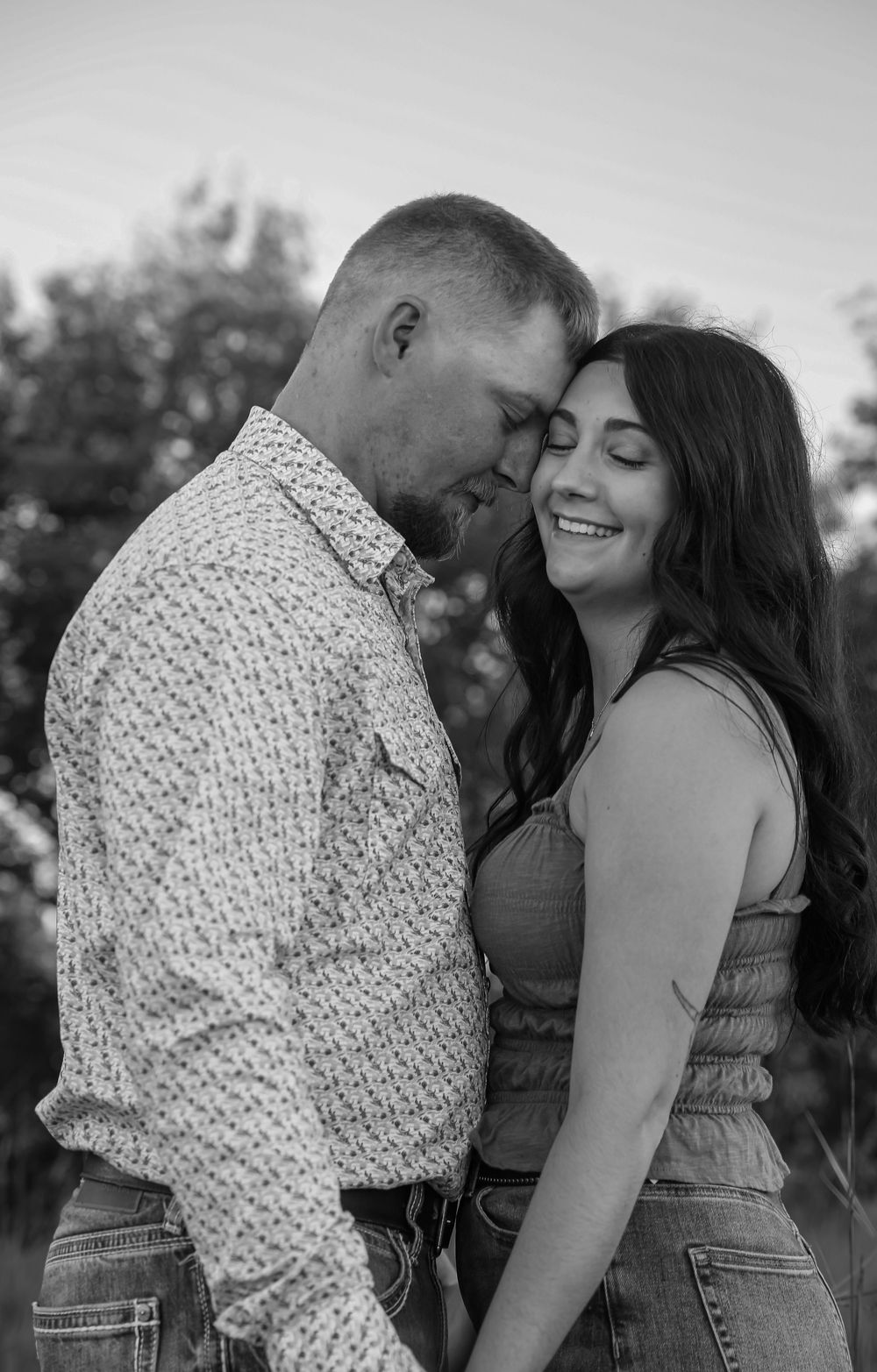 Black and white photo of a smiling couple touching foreheads in an outdoor setting.