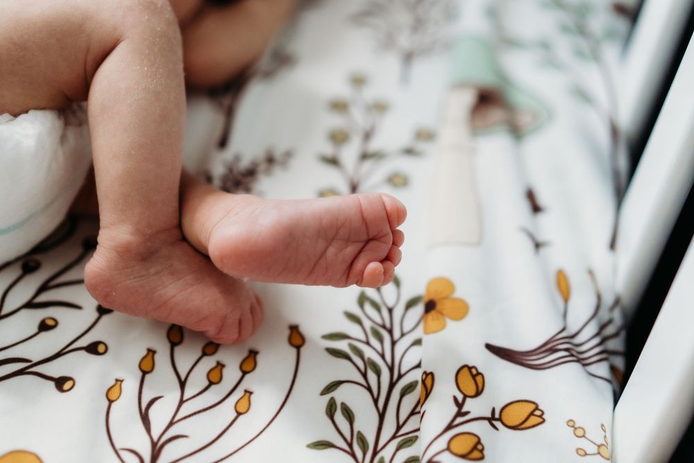 Close-up of newborn baby feet resting on a floral patterned white blanket in a crib.