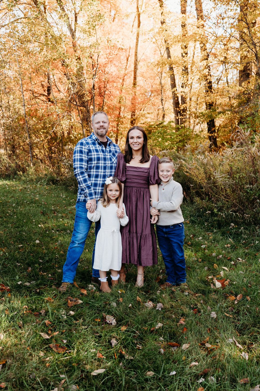 Family of four posing in autumn forest with vibrant orange foliage during fall family portrait session.
