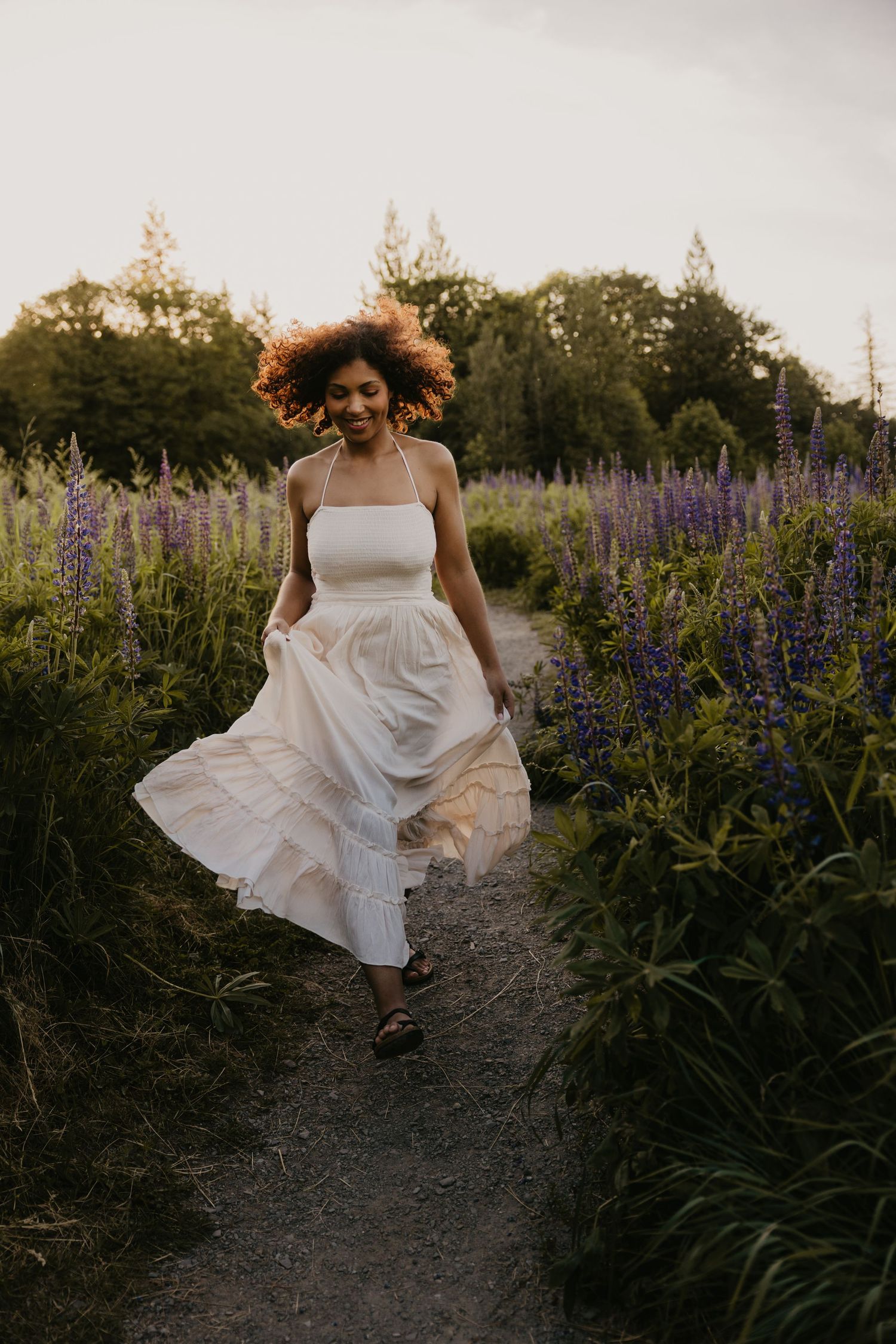 Woman in a flowy dress walking through purple lupine flower field at golden hour sunset in Washington.