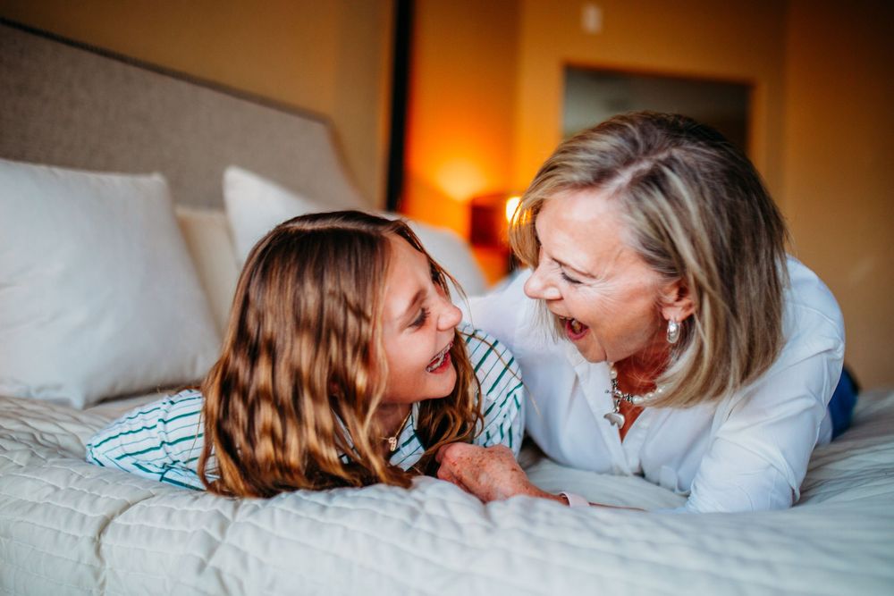 A grandmother and young girl laughing together while lying on a hotel bed, sharing a joyful moment.