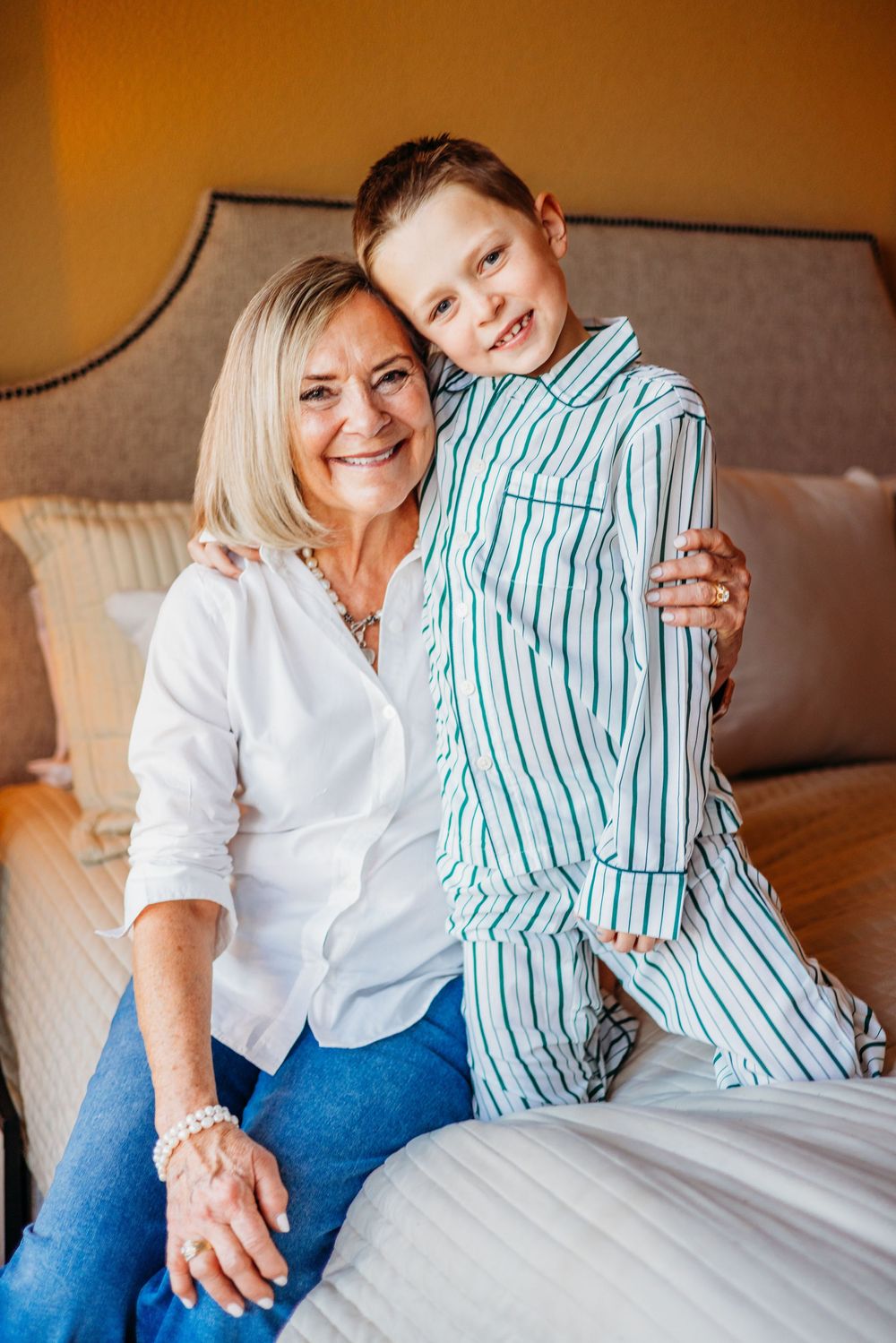Grandmother and young boy in striped pajamas sitting together on a bed, smiling warmly.