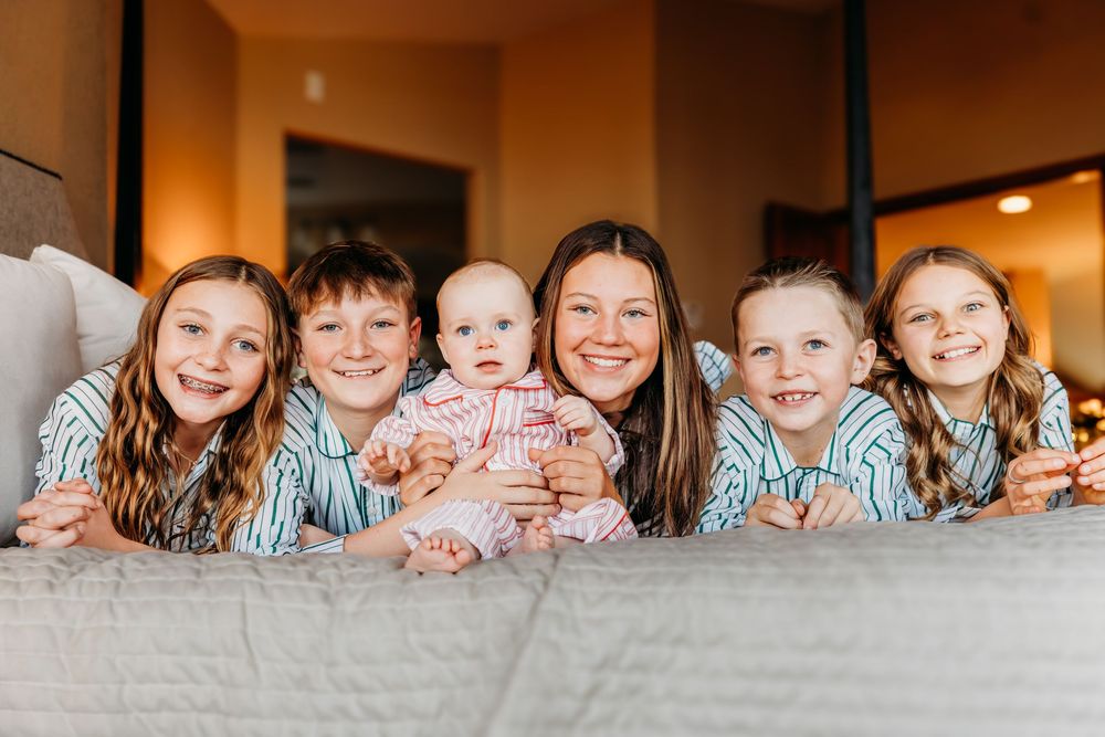 A smiling mother and four children lying on a bed, posing together for a cheerful family portrait photo.