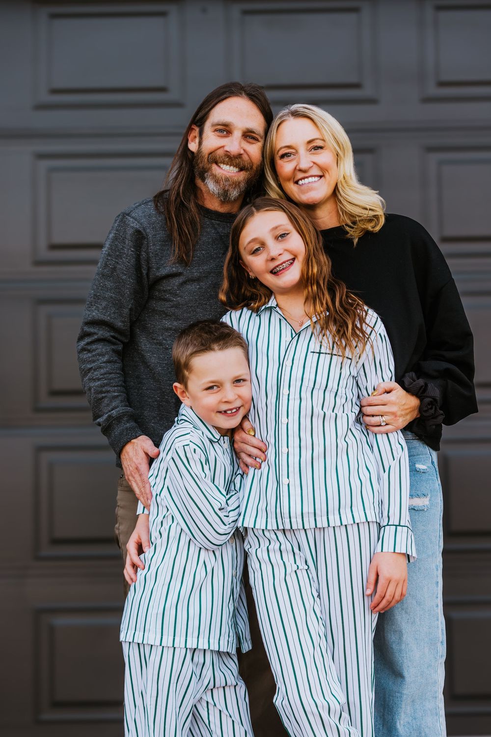 Happy family of four posing together outdoors, two children wearing matching striped pajamas.