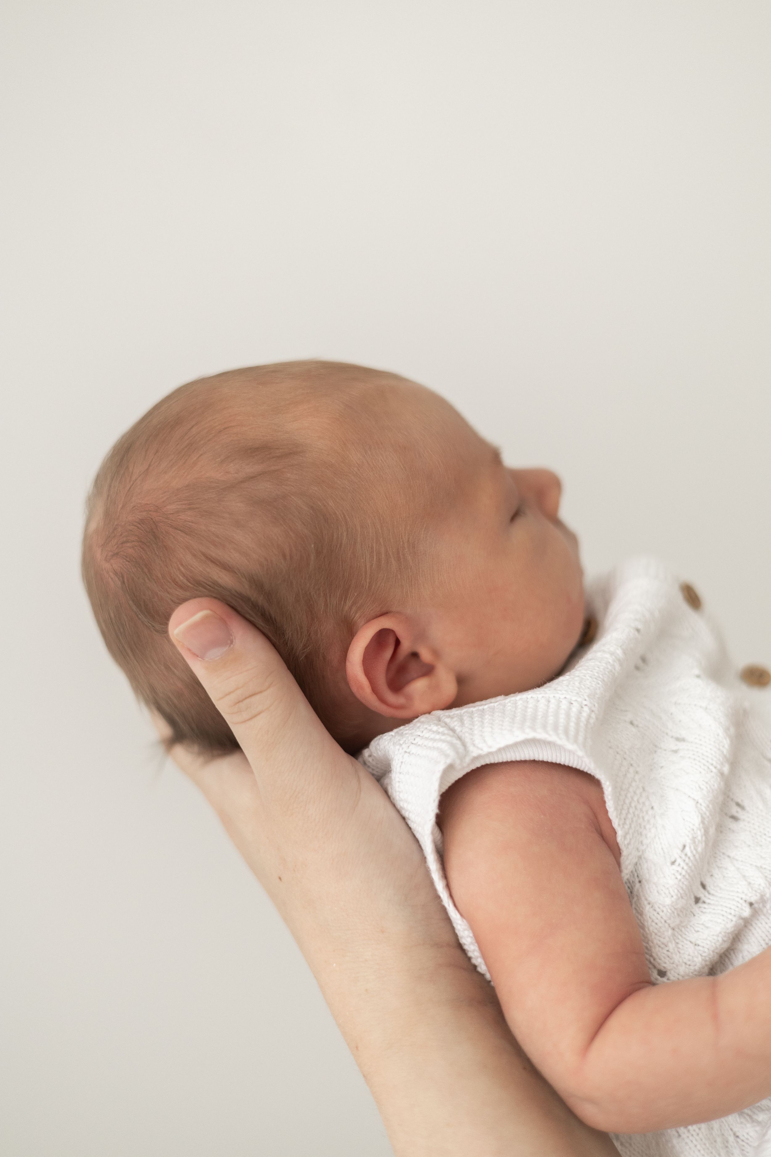 A newborn baby in a white onesie being cradled in mums hand, Nottingham newborn photographer