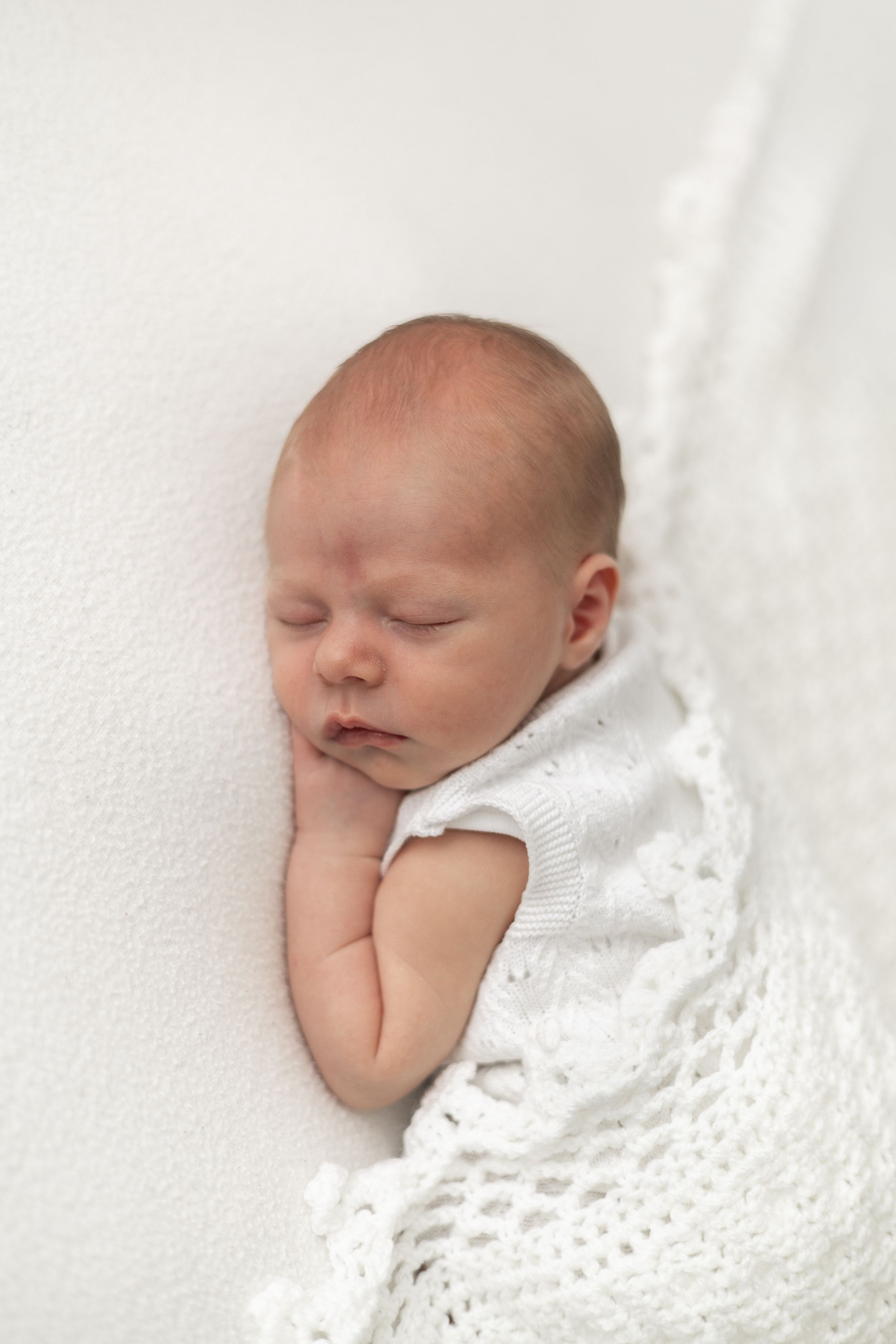 Peaceful newborn baby sleeping on white blanket wearing a white knit romper in a calm Nottingham newborn studio